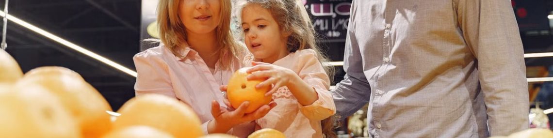 Parents and child selecting fresh oranges together at the supermarket. Captures family bonding and healthy shopping.
