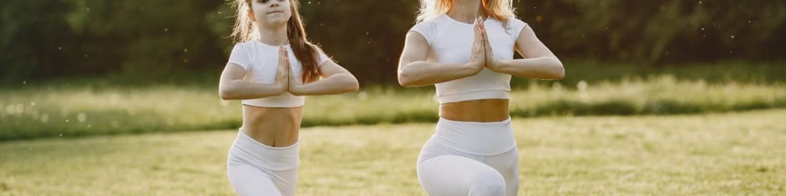 A mother and daughter practicing yoga together in matching outfits in a sunny park.