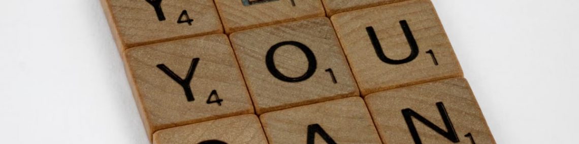 Wooden Scrabble tiles on white surface spelling 'Yes You Can,' promoting positivity and motivation.